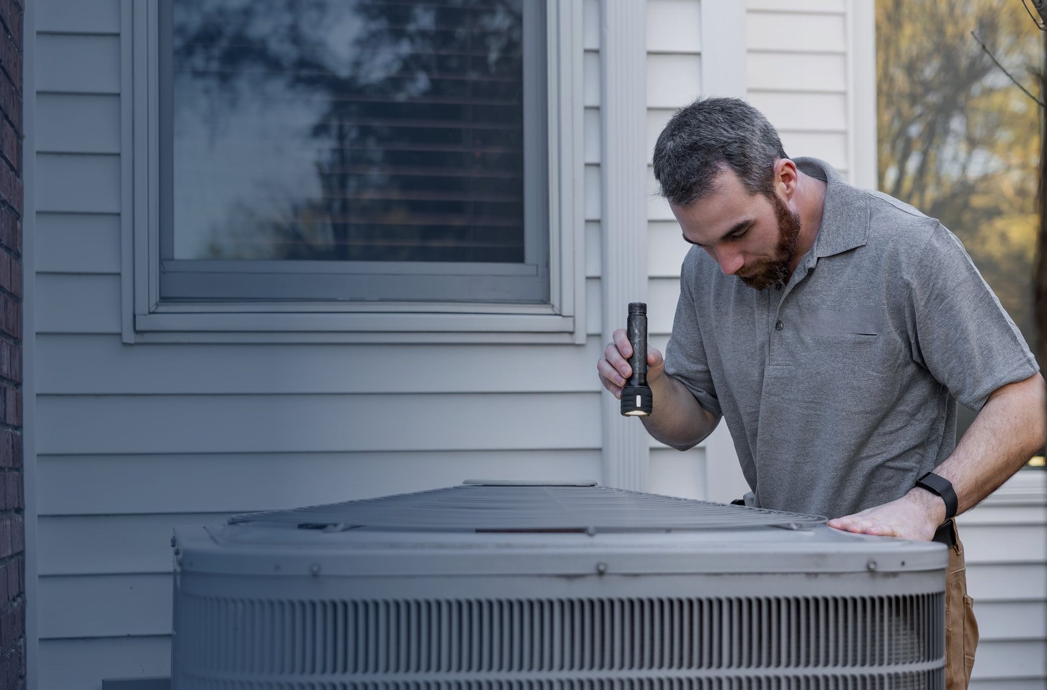 A technician inspecting an outdoor air conditioning condenser at a home
